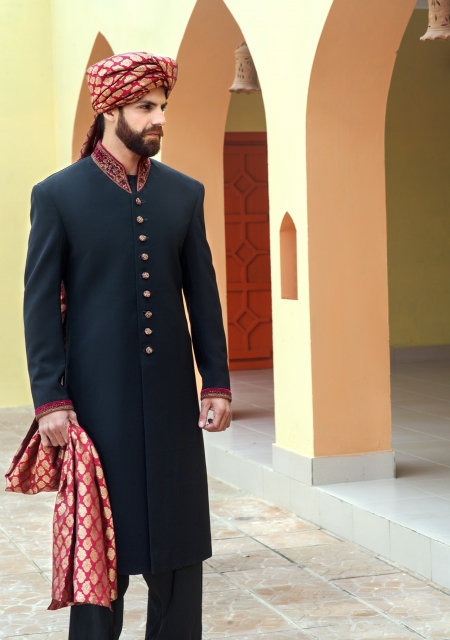 a bearded man in a black sherwani.